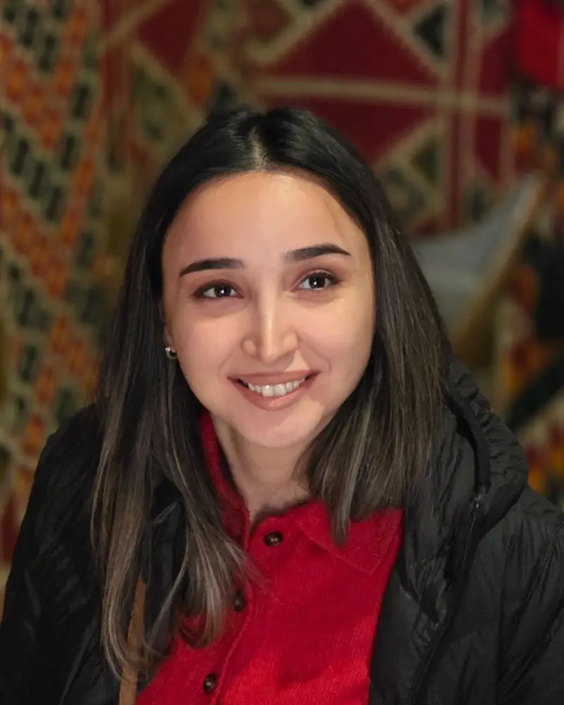 Portrait of Gunel smiling in front of a patterned carpet